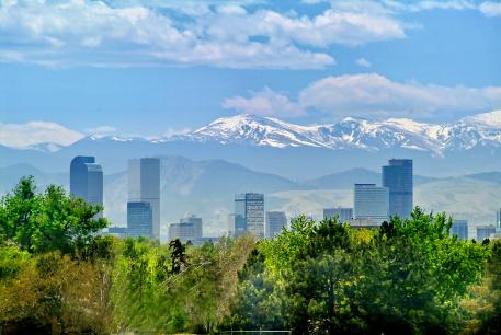 Skyline of Denver, Colorado on a bright sunny day with a blue sky. Mountains in the background and trees in the foreground